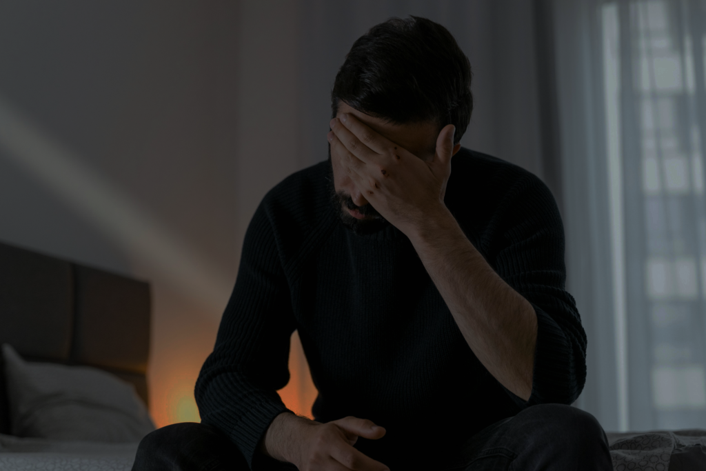 Man sitting on end on the bed with hand over his head